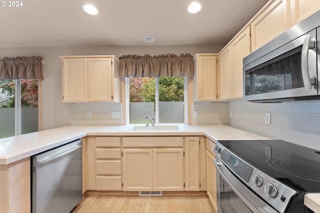 kitchen with sink, backsplash, kitchen peninsula, stainless steel appliances, and light hardwood / wood-style flooring