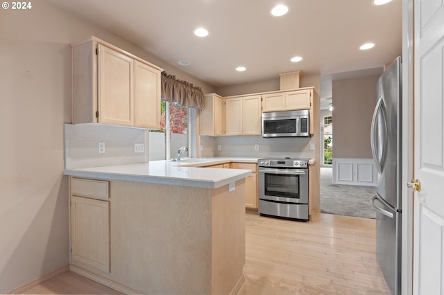 kitchen with sink, appliances with stainless steel finishes, kitchen peninsula, and light wood-type flooring