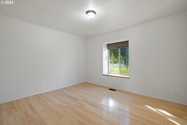 unfurnished room featuring a textured ceiling, light wood-type flooring, and crown molding