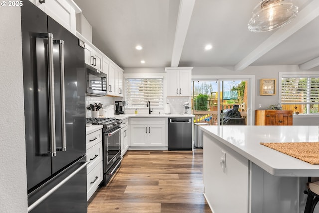 kitchen featuring beam ceiling, white cabinetry, sink, and premium appliances