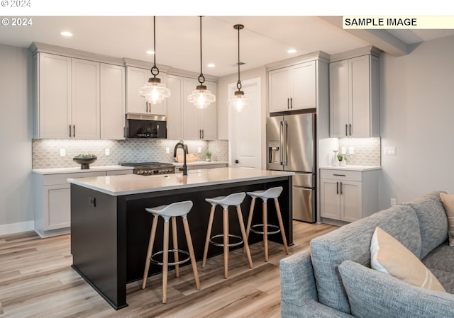 kitchen featuring pendant lighting, stainless steel appliances, a kitchen island with sink, and light hardwood / wood-style flooring