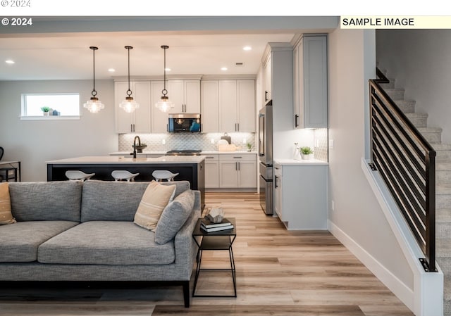 kitchen with sink, an island with sink, decorative light fixtures, appliances with stainless steel finishes, and light wood-type flooring