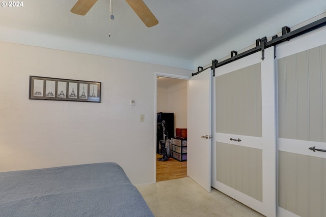 bedroom featuring a barn door, ceiling fan, and light colored carpet