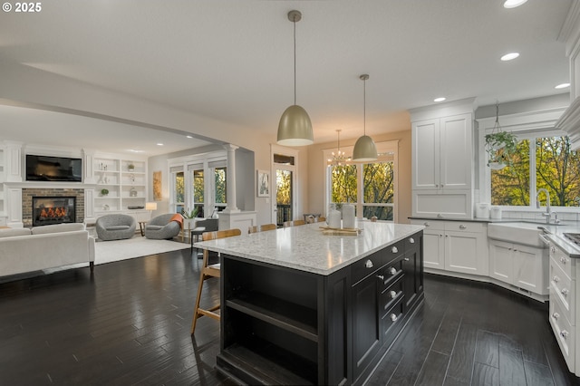 kitchen featuring white cabinetry, a center island, sink, pendant lighting, and a fireplace