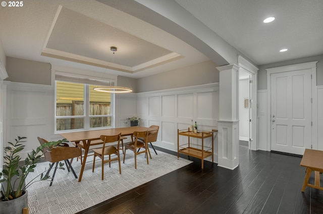 dining space featuring dark hardwood / wood-style floors, ornate columns, crown molding, and a tray ceiling