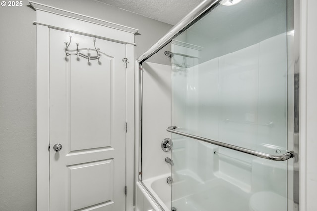 bathroom featuring combined bath / shower with glass door and a textured ceiling