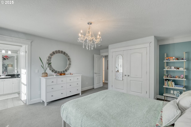 carpeted bedroom with ensuite bath, sink, a textured ceiling, and an inviting chandelier