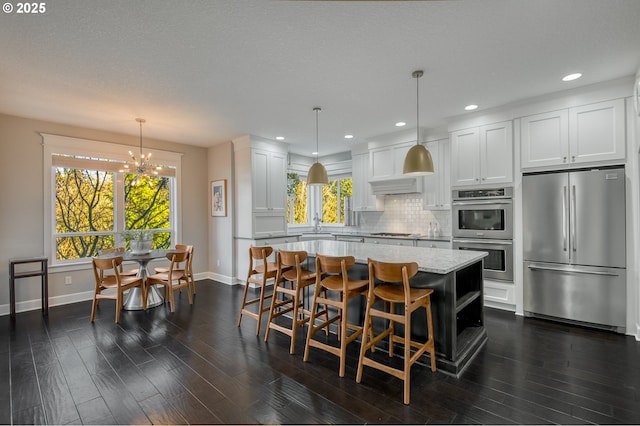 kitchen with backsplash, hanging light fixtures, a kitchen island, white cabinetry, and stainless steel appliances