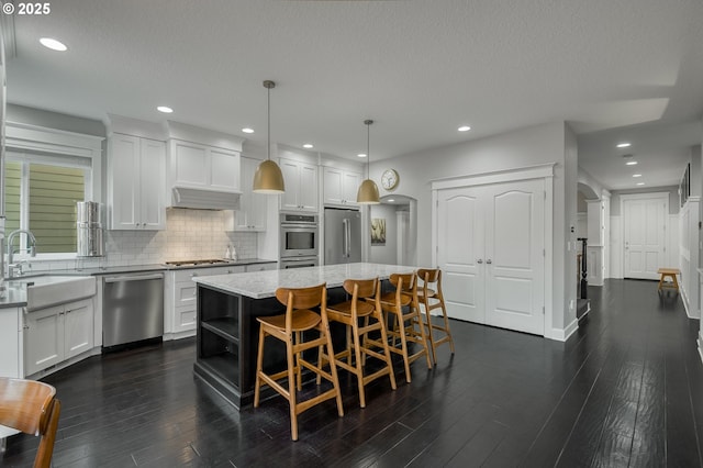 kitchen featuring stainless steel appliances, sink, white cabinets, a kitchen island, and hanging light fixtures