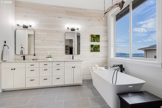 bathroom with wood walls, a freestanding bath, double vanity, tile patterned floors, and a sink