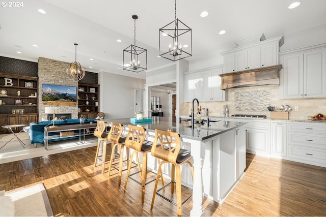 kitchen with a fireplace, a sink, white cabinets, light wood-style floors, and under cabinet range hood