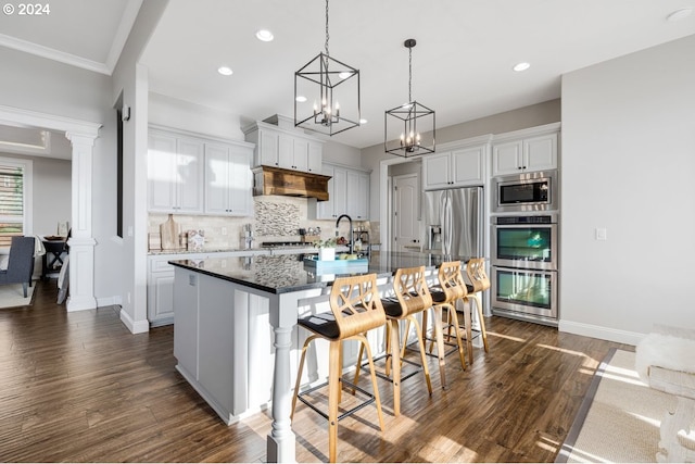 kitchen with a kitchen island with sink, dark wood-style flooring, stainless steel appliances, a kitchen bar, and tasteful backsplash