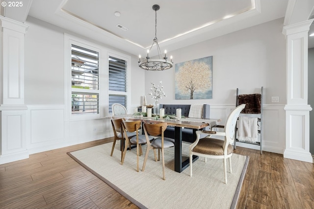 dining space featuring dark wood finished floors, a tray ceiling, and ornate columns