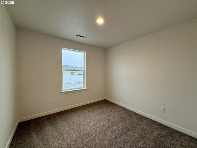 empty room with dark carpet, visible vents, and baseboards