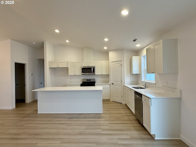 kitchen with visible vents, lofted ceiling, a kitchen island, appliances with stainless steel finishes, and light wood-style floors