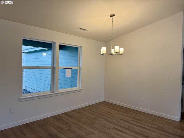 empty room featuring dark wood-style floors, a chandelier, visible vents, and baseboards