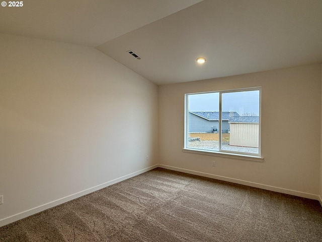 spare room featuring dark colored carpet, visible vents, vaulted ceiling, and baseboards