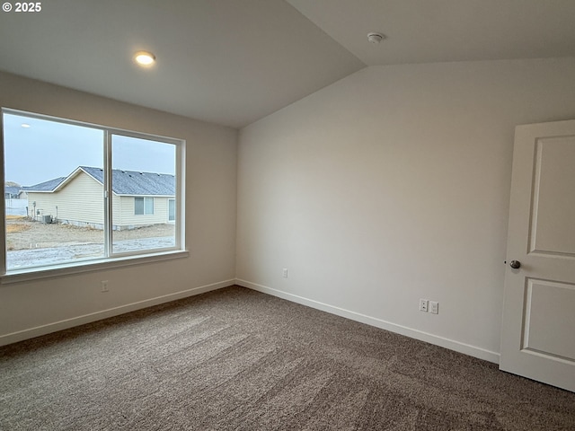 empty room featuring vaulted ceiling, baseboards, and dark colored carpet