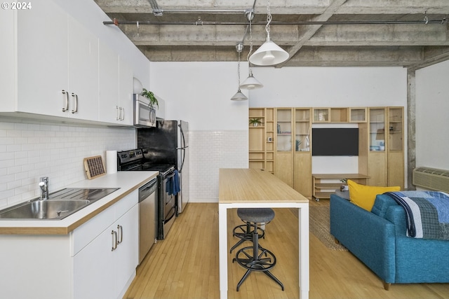 kitchen with appliances with stainless steel finishes, light wood-type flooring, sink, white cabinetry, and hanging light fixtures