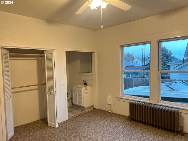 unfurnished bedroom with ceiling fan, carpet floors, sink, and radiator