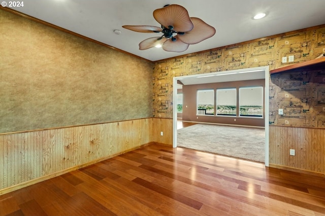 empty room with wooden walls, crown molding, ceiling fan, and wood-type flooring