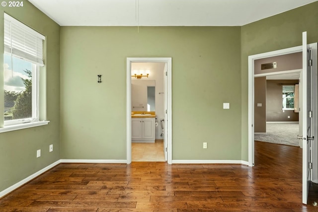 unfurnished bedroom featuring connected bathroom, multiple windows, and dark hardwood / wood-style floors