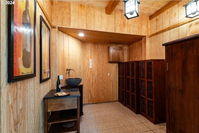 hallway featuring beamed ceiling, wood walls, and light tile patterned flooring