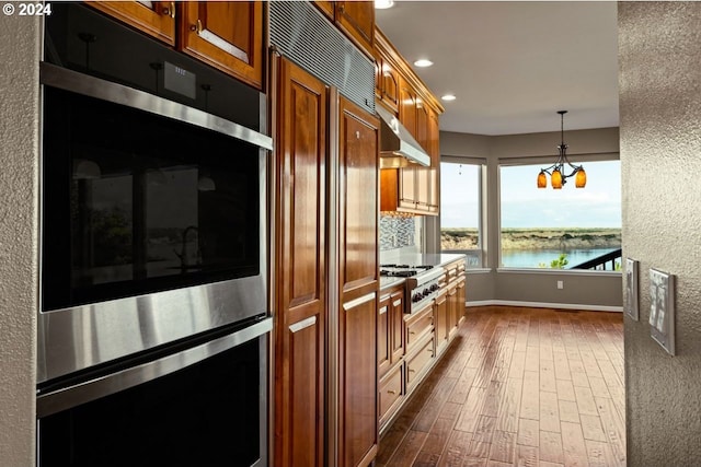 kitchen with dark hardwood / wood-style flooring, stainless steel appliances, pendant lighting, a water view, and range hood