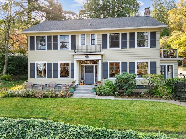 colonial-style house featuring a balcony and a front yard