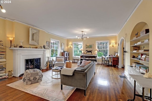 living room featuring hardwood / wood-style flooring, crown molding, built in shelves, and an inviting chandelier