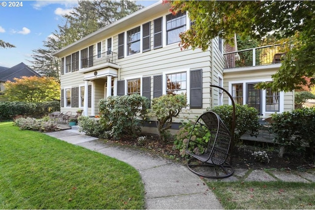 colonial inspired home featuring a balcony and a front lawn