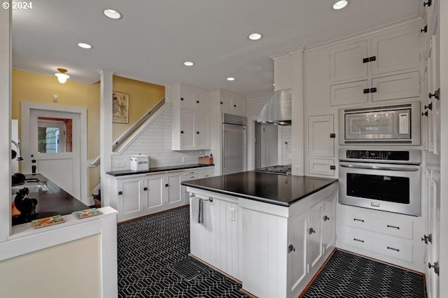 kitchen featuring white cabinetry, built in appliances, backsplash, and wall chimney exhaust hood