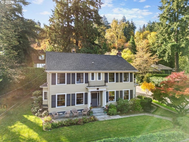 colonial house with a balcony, a patio, and a front yard