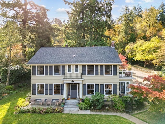 colonial house with a front yard, a patio, and a balcony