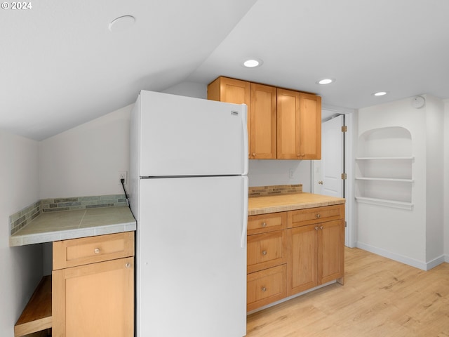 kitchen with tile countertops, lofted ceiling, white fridge, and light hardwood / wood-style floors