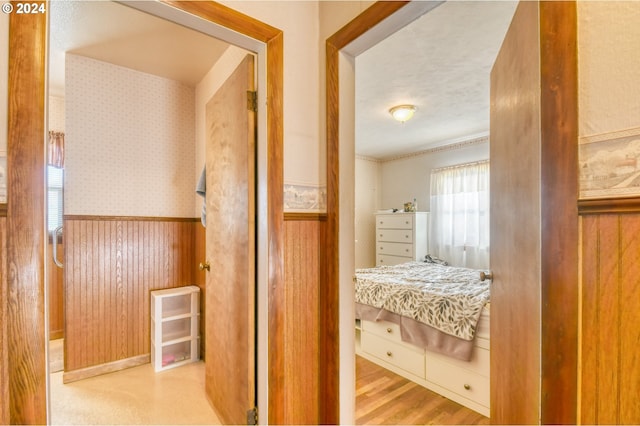 hallway with light hardwood / wood-style floors, a textured ceiling, and wooden walls