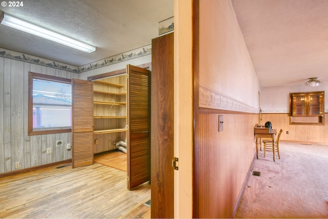 interior space featuring a textured ceiling, light wood-type flooring, lofted ceiling, and wood walls