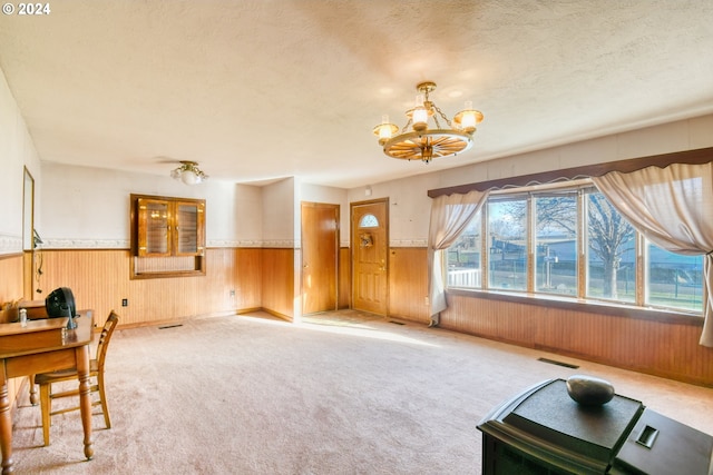 interior space featuring carpet flooring, wood walls, a textured ceiling, and a chandelier