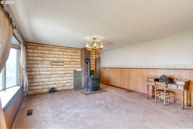 unfurnished living room featuring a wood stove, light carpet, log walls, and an inviting chandelier