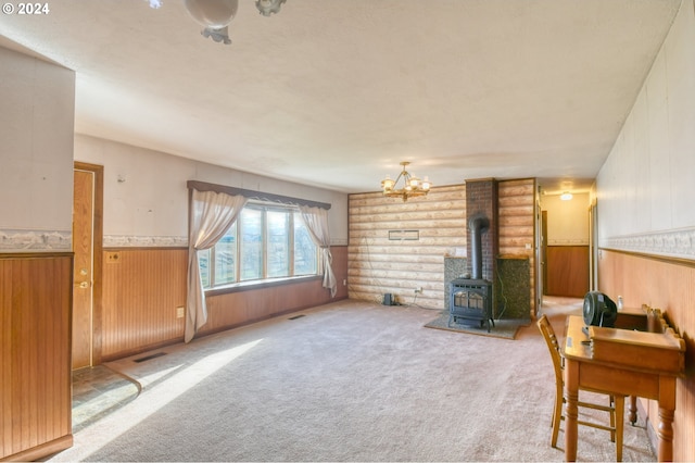 carpeted living room featuring a wood stove, wood walls, and a chandelier