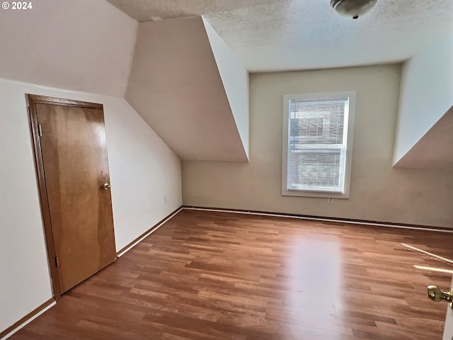 additional living space with hardwood / wood-style flooring, a textured ceiling, and lofted ceiling