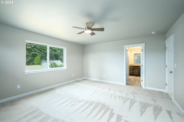 unfurnished bedroom with ceiling fan, ensuite bathroom, and light carpet