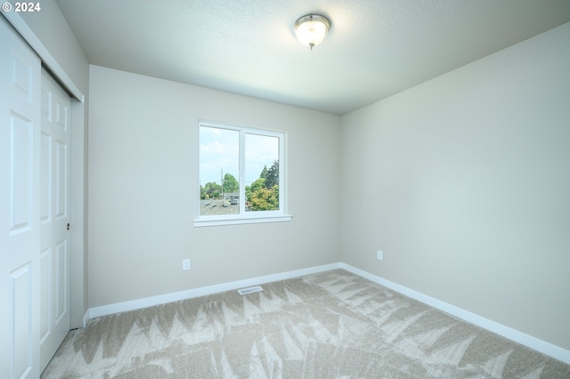 unfurnished bedroom with light colored carpet and a closet