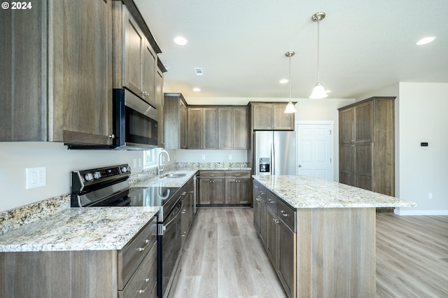 kitchen with a center island, appliances with stainless steel finishes, hanging light fixtures, sink, and light hardwood / wood-style flooring