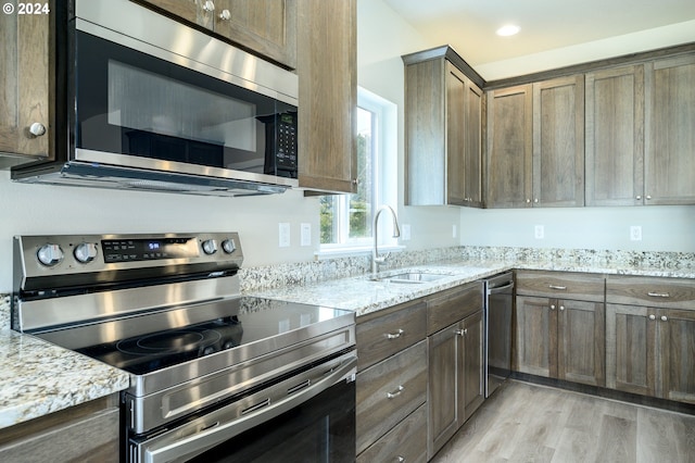 kitchen featuring light stone countertops, light hardwood / wood-style floors, appliances with stainless steel finishes, and sink