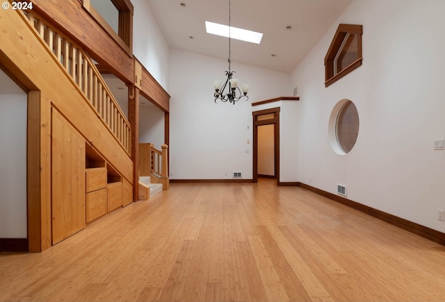 unfurnished room with an inviting chandelier, light hardwood / wood-style flooring, high vaulted ceiling, and a skylight