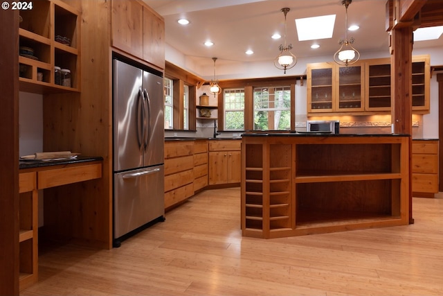 kitchen featuring a skylight, light wood-type flooring, decorative light fixtures, and appliances with stainless steel finishes