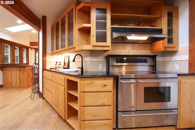 kitchen with stainless steel range with electric stovetop, dark stone countertops, backsplash, and light hardwood / wood-style flooring