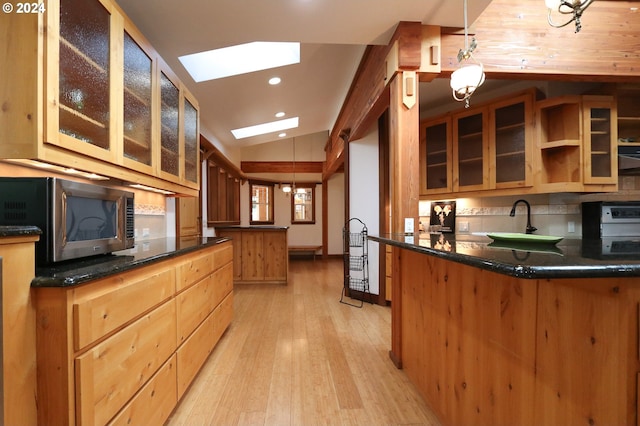 kitchen with sink, vaulted ceiling with skylight, hanging light fixtures, and light hardwood / wood-style floors