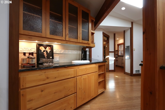 bar with decorative backsplash, light wood-type flooring, lofted ceiling, and dark stone countertops